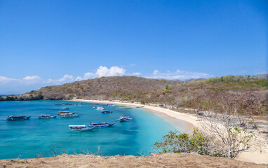 A view on a bay on Pink Beach, Lombok Indonesia. Plenty colourful boats anchored to the shore. The water has many shades of blue. The heavenly beach is surrounded by small hills. Paradise beach.