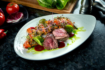Medium rare beef medallions with vegetable garnish, served on a white plate. Dark marble background. Barbecue meat, restaurant food. Tasty steak
