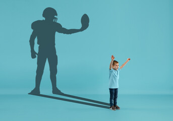 Childhood and dream about big and famous future. Conceptual image with boy and shadow of male american football player, champion on blue background. Dreams, imagination, education concept.