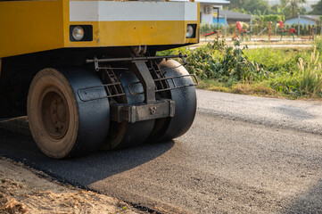 Yellow steamroller or soil compactor working on asphalt road at construction site
