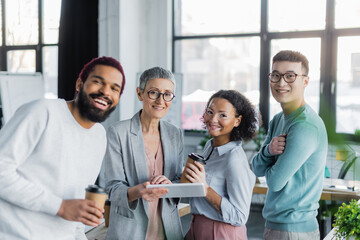 Interracial business people with paper cups and digital tablet smiling in office