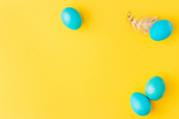 Easter frame made of blue eggs and feather on yellow background. Festive arrangement for Easter greeting card or hunt invitation.