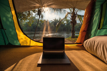 Modern laptop open and put down inside a camping tent in natural park