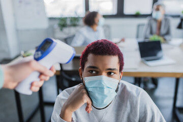 African american businessman in medical mask near colleague with non-contact thermometer
