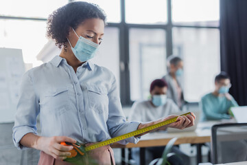 African american businesswoman in medical mask holding tape measure