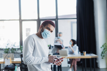 African american businessman in medical mask using digital tablet in office