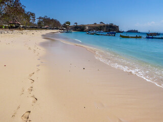 An areal, drone shot with a view on an idyllic Pink Beach on Lombok, Indonesia. Many boats drifting on a calm surface of the sea. Unspoiled, hidden gem. Perfect place for peaceful, relaxed holidays