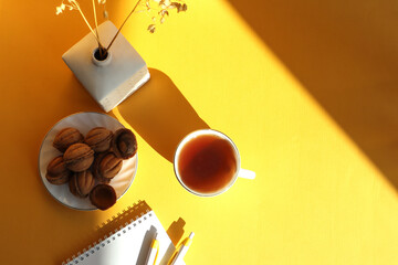 Baked cookies, a cup of tea, a bouquet of dried cereals, a notepad and a pen on a yellow background with its own shadow, a top view, a place for text