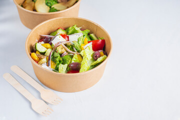 Diet Greek salad with feta, tomatoes, greens on light background top view. Healthy lunch. Food delivery in disposable plate of craft paper. Eco-friendly carton packaging environment protection