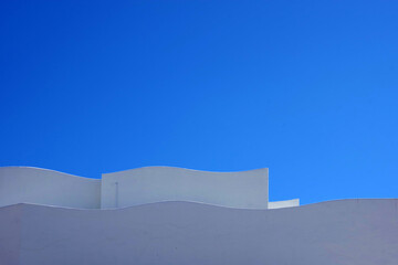 Partial view of the wave shaped top of a large white building complex and blue sky above