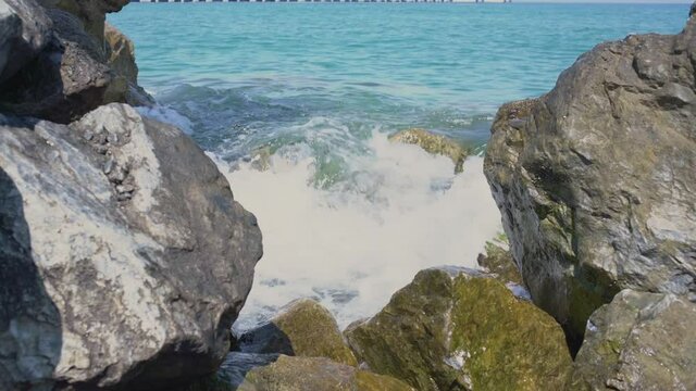 Sea wave with force breaks on large coastal stone forming splashes and white foam.
