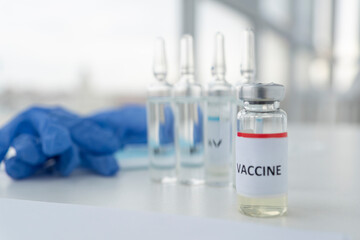 close up image of vial with inscription vaccine, other three ampoules and blue medical gloves not in focus. Healthcare and vaccination concept