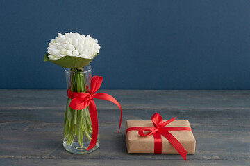 Little bouquet of white snowdrops in vase tired up with red ribbon, wrapped gift box is near on dark wooden background. Greeting concept. Celebration of spring holidays.