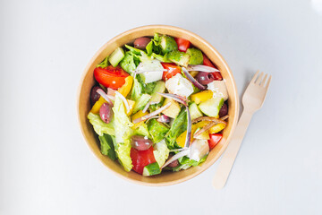 Diet Greek salad with feta, tomatoes, greens on light background top view. Healthy lunch. Food delivery in disposable plate of craft paper. Eco-friendly carton packaging environment protection