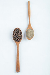 Grain peppers and ground pepper on wooden spoon