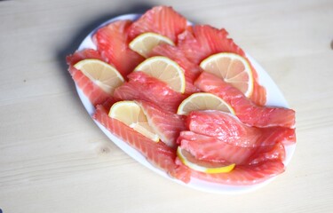 slices of salty red fish salmon with lemon on white plate on wooden background