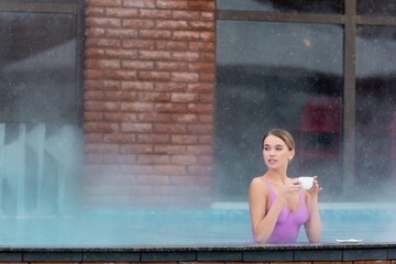 young woman holding cup of coffee in outdoor swimming pool