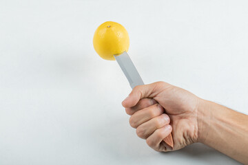 Hand holding a knife with a whole lemon on white background