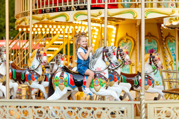 happy baby girl rides a carousel on a horse in an amusement Park in summer