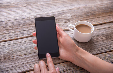 Smartphone in female hands on the background of a wooden table and a cup of coffee.