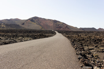 Empty road at Timanfaya National Park volcanic landscape. Nobody on sight on sunny day at tourist attraction landmark in Canary Islands, Spain. Uncertainty, unknown destination, explore concepts