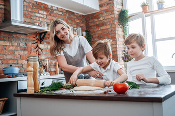 Atmospheric portrait of a two preschool boys with their joyful mother they enjoy their leisure together in kitchen.
