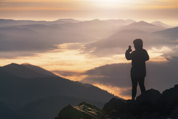 Obraz premium Young girl on the mountain peak photographs mountain landscape on the phone.