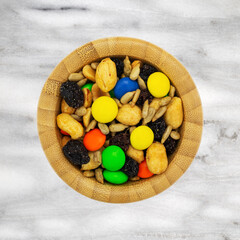 Top view of a portion of sweet and salty trail mix in a wood bowl on a marble countertop.