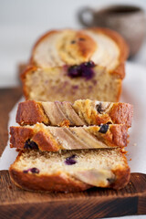 Banana bread, slice of cake with banana and blueberries. Morning breakfast with coffee on light gray linen textile tablecloth on table, Lifestyle still life food. Side view. Close up, macro, vertical