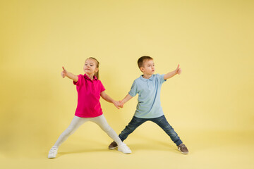 Jumping, dancing. Childhood and dream about big and famous future. Pretty little kids isolated on yellow studio background. Dreams, imagination, education, facial expression, emotions concept.