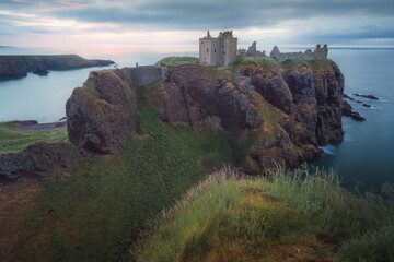 Fototapeta na wymiar Moody, dramatic sunset or sunrise sky over the medieval ruins of a Dunnottar Castle on the Aberdeenshire coast on the North Sea in Scotland.