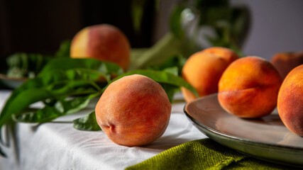 Peaches on table in kitchen near window. Rustic minimalism food peach fruits with leaves on wooden board on tablecloth. Harvest of Ripe juicy peaches. Long web banner