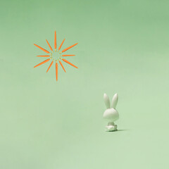 Spring concept for Eastern. A rabbit sitting and staring in pastel green distance. Photo of bunny’s back. Carrots on the top.