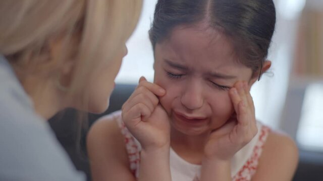 Pretty little girl cries while sitting on the sofa.Loving mother trying to calm her sad crying little daughter. Portrait of really crying little girl. Slow motion and close up video.