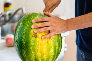 Closeup of young man at home holding cutting in half watermelon with knife and fruit has yellow field spot indicating sweetness - Powered by Adobe