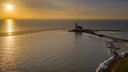 Winter landscape at the Lighthouse Paard van Marken Netherlands. On a cold day, temperature -7 degree during sunset. The IJsselmeer is frozen and by strong wind the shore was covered with ice