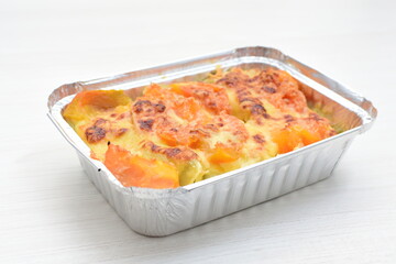Baked chicken and mushroom cannelloni, bathed in cream in cheese sauce gratin on white wooden background