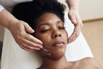 A young black woman lies in the beautician's office and relaxes from gentle touches and toning massage. The concept of spa treatments