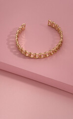 Top view of chain shape golden bracelet on pink background with copy space