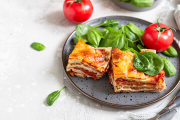 Italian lasagna with tomato sauce and cheese served with tomatoes and spinach, light concrete background. Homemade vegetarian lasagna.