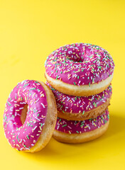 Pink glaze donuts with colorful sprinkles on yellow background. Minimalist concept.