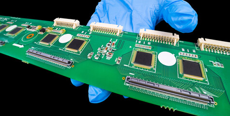 Long electronic printed circuit board on hand in blue glove isolated on a black background....