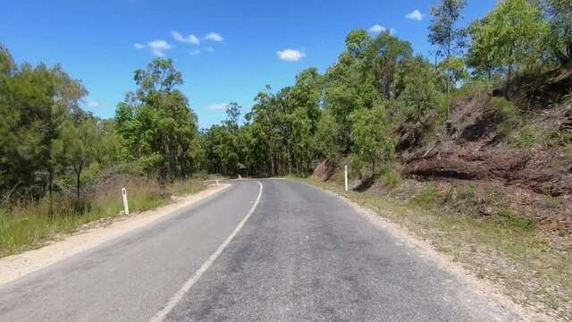 Rear facing driving point of view POV of a deserted dry dusty Queensland country road with gum trees and rocky banks - ideal for interior car scene green screen replacement