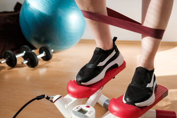 Close woman legs doing cardio on the stepper and using elastic bands with ball, and dumbbells on...