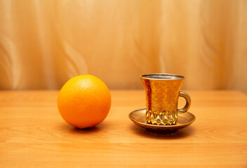 Orange is near the golden cup, golden background, table