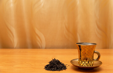 Golden cup for tea. On the golden background, orange table. Golden curtain.