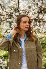 girl in a corduroy jacket looks aside in the garden or park near a blossoming apple tree apricot tree in spring