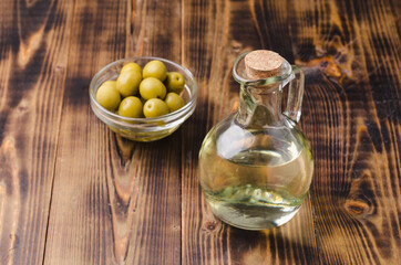 Olive oil in a bottle and fruits of olives in a bowl. Olive oil bottle and olives on wooden background with copy space.