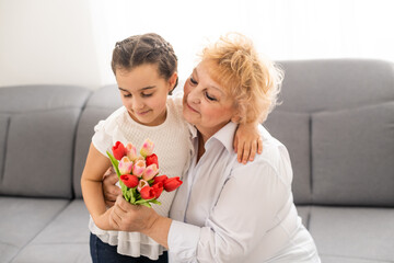 Fototapeta na wymiar Little beautiful granddaughter gives her grandmother a bouquet of pink tulips. The concept of family, respect, generation, mother, upbringing
