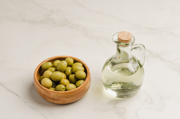 Bottle of olive oil and olives in a wooden bowl. Olive oil bottle and olives on white stone table